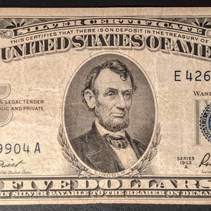 May include: A vintage five dollar bill featuring a portrait of Abraham Lincoln. The bill is in good condition and has a serial number of E 42659904 A. The text "This certifies that there is on deposit in the Treasury of the United States of America" is printed at the top of the bill.
