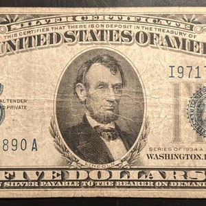 May include: A vintage five dollar bill from the United States of America, featuring a portrait of Abraham Lincoln. The bill is dated 1934 and has the serial number 197174890 A.