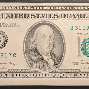 May include: A US $100 bill featuring a portrait of Benjamin Franklin. The bill has a green serial number, B 30097917 C, and the text "THE UNITED STATES OF AMERICA" printed in black.