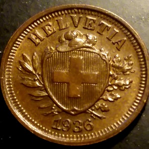 May include: A bronze Swiss coin with the inscription "HELVETIA" and the year "1936". The coin features a shield with a cross and is surrounded by a wreath.