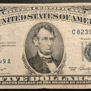 May include: A vintage five-dollar silver certificate from the United States of America. The bill features a portrait of Abraham Lincoln and ornate scrollwork. The text includes "FIVE DOLLARS" and "SILVER PAYABLE TO THE BEARER ON DEMAND."