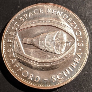 May include: A silver commemorative coin with the text "First Space Rendezvous Stafford - Schirra" and a depiction of a spacecraft.