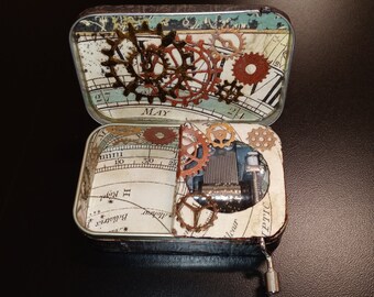 May include: Open metal box with a vintage map design, featuring decorative gears and a small music box mechanism. The box is open, revealing the interior details and the word "May" on the lid.
