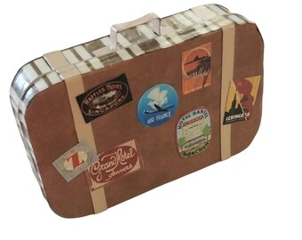 May include: A brown rectangular suitcase with a top handle and light-colored straps. The surface features vintage-style travel stickers including Raffles Hotel Singapore, Air France, Hotel Danieli Munchen, Grand Hotel Anvers, and Leningrad.