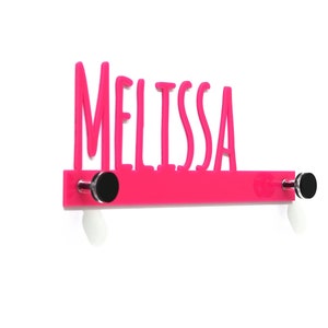 May include: A pink acrylic nameplate with the name "Melissa" in white lettering. The nameplate has two silver hooks with black caps on each end.