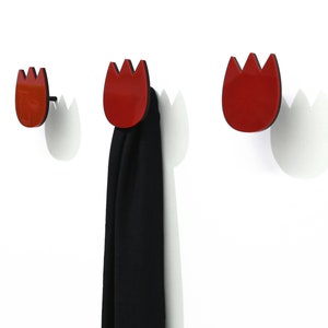 Può includere: Tre ganci rossi a forma di tulipano montati su una parete bianca. Un gancio ha una sciarpa nera appesa.