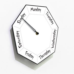 May include: A white octagonal clock with black hands and black lettering. The clock face displays the days of the week: Sunday, Monday, Tuesday, Wednesday, Thursday, Friday, Saturday.