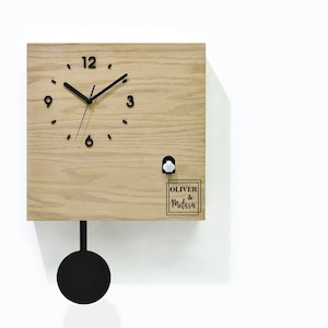 May include: A wooden cuckoo clock with a black pendulum and a white cuckoo bird. The clock face has black Roman numerals and black hands. The clock is personalized with the names "Oliver & Melissa".