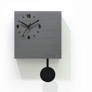 May include: A grey wooden square clock with black hands and numbers. The clock has a pendulum and is hanging on a white wall. The text "Cuckoo Clocks Time Box by Sol Pixie Dust" is visible in the bottom right corner of the image.