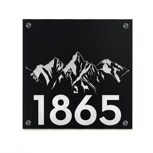Peut inclure: Plaque de numéro de maison en métal noir avec un motif de chaîne de montagnes argenté et le numéro 1865 en argent.