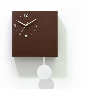 May include: A brown wooden cuckoo clock with a white pendulum and white clock hands. The clock face has black Roman numerals and a white bird illustration in the bottom right corner. The text "Cuckoo Clocks Time Box by Sol Pixie Dust" is below the bird.