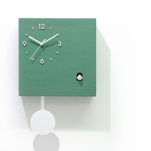 May include: A green square cuckoo clock with white hands and numbers. The clock has a white pendulum and a small white bird that pops out of the hole on the front of the clock. The clock is made by Time Box.