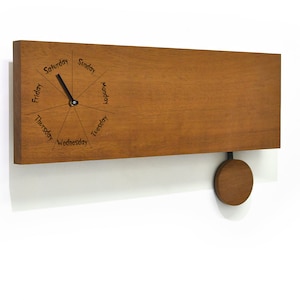May include: A wooden wall clock with a pendulum. The clock face features the days of the week in a circular pattern. The clock is made of light brown wood.
