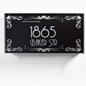 May include: Black metal mailbox with a silver design. The mailbox has the number 1865 and the street name "Baker Str" on it.