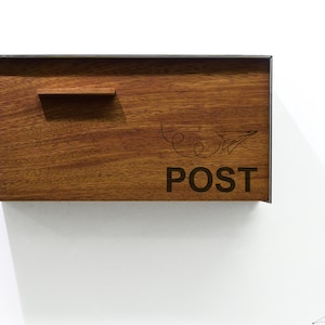 Cassetta postale con frontale in legno massello di Iroko - Corpo in alluminio grigio metallizzato - Numero dell'aereo di carta inciso al laser - Montaggio a parete Mailnest Style 3