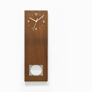 Peut inclure: Une horloge murale en bois brun avec un cadran blanc et des aiguilles blanches. L'horloge a une petite fenêtre circulaire dans la moitié inférieure du cadran.