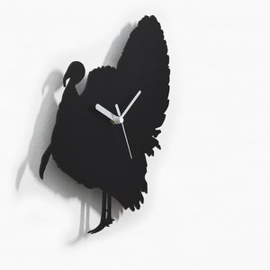 May include: Black silhouette wall clock shaped like a turkey with white clock hands. The clock is on a white wall. By Sol Pixie Dust.