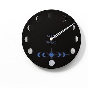 Op de afbeelding: Een zwarte ronde klok met witte wijzers en een wit maanfasenontwerp. De wijzerplaat van de klok heeft de tekst "Moon Phases" in witte letters.