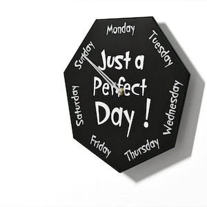 May include: Black octagonal clock with white text that reads "Just a Perfect Day!" and the days of the week around the edge. The clock hands are pointing to Sunday.