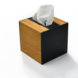 May include: A wooden tissue box with a black top and a white tissue inside. The box has a wood grain pattern and a black trim.