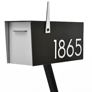 May include: A black and white modern mailbox with a silver flag and the house number 1865 on the front.