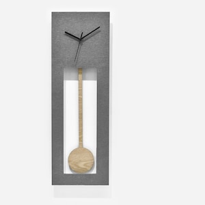 Peut inclure: Une horloge murale rectangulaire grise avec un pendule en bois et des aiguilles noires. Le cadran de l'horloge est visible à travers une découpe dans la surface grise.