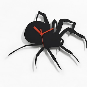 May include: Black spider-shaped wall clock with red clock hands. The clock is made of metal and has a minimalist design.