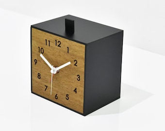 May include: A black wooden clock with a wood-grain face and white hands. The clock face has black numbers from 1 to 12. The clock is on a white surface. The text "ZZ Z" and "By Sol Pixie Dust" is below the clock.