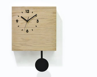 Puede incluir: Un reloj cuadrado de madera con un péndulo negro y agujas negras. La esfera del reloj tiene números negros y está configurado a las 12:00. El reloj está hecho por Cuckoo Clocks Time Box & Sol Pixie Dust.
