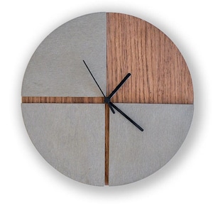 Puede incluir: Un reloj redondo de madera gris y marrón con manecillas negras. El reloj está dividido en cuatro secciones, con dos secciones grises y dos secciones de madera marrón.