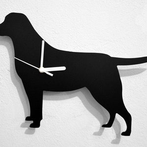 May include: Black silhouette of a Labrador Retriever dog with white clock hands. The clock is mounted on a white wall.