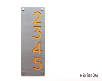 May include: A gray metal house number sign with the numbers 2, 3, 4, and 5 cut out in a bright orange color. The numbers are arranged vertically.
