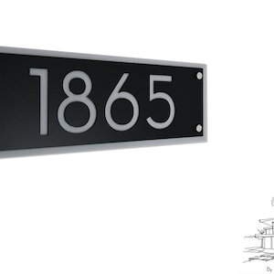 Könnte beinhalten: Ein schwarzes und graues Hausnummernschild mit der Nummer 1865 in Weiß. Das Schild ist aus Acryl und hat ein modernes Design.