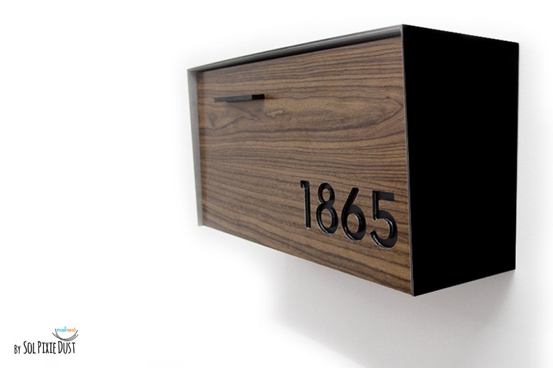 May include: A wooden mailbox with a black metal frame and a black metal handle. The mailbox has a wood grain pattern and the number 1865 is cut out of the wood.