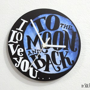Puede incluir: Un reloj blanco y negro con un diseño de luna azul en acuarela. La esfera del reloj dice "I Love You To The Moon And Back".