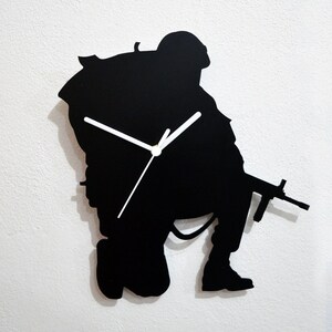 May include: Black silhouette wall clock shaped like a soldier holding a rifle. The clock has white hands.