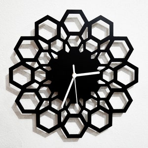 May include: Black clock with a honeycomb design and white hands. The clock is made of metal and has a modern design.
