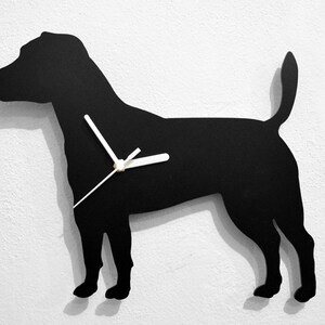 May include: Black silhouette of a dog with white clock hands. The dog is standing on a white wall.