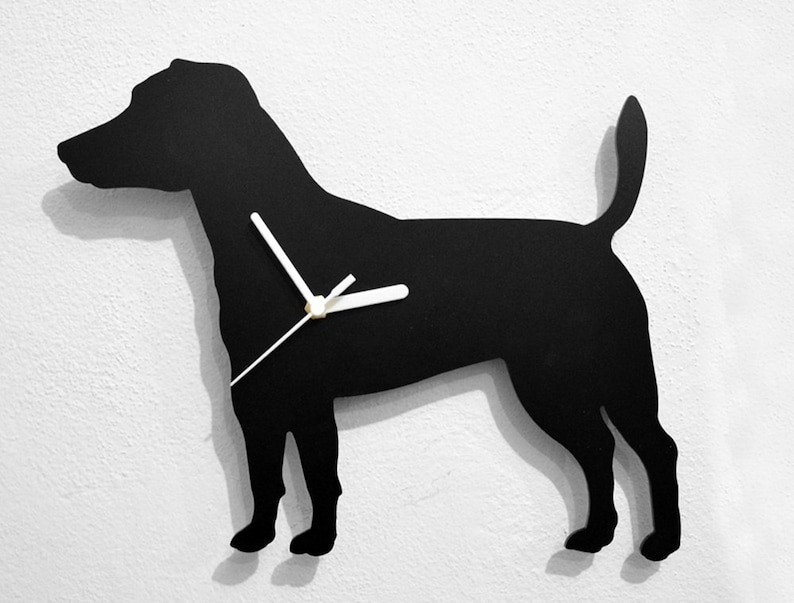 May include: Black silhouette of a dog with white clock hands. The dog is standing on a white wall.