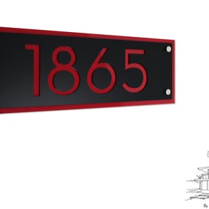 Könnte beinhalten: Ein schwarzes Hausnummernschild mit rotem Rand und der Nummer 1865 in Rot.
