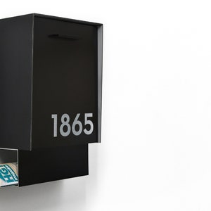 May include: A black metal mailbox with a slot for mail and a separate compartment for newspapers. The mailbox has the number 1865 printed on the front.