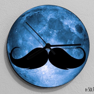 Puede incluir: Un reloj de luna azul con una silueta de bigote negro. La esfera del reloj es una imagen de cerca de la superficie de la luna.