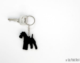 May include: Black silhouette of a dog on a silver key chain. The keychain has a silver key attached to it.