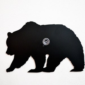 May include: Black metal silhouette of a bear walking, mounted on a white wall.