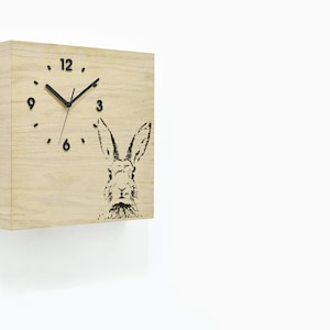 May include: A wooden wall clock with a black rabbit silhouette and black clock hands. The clock face has black Roman numeral markings.