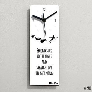 Puede incluir: Un reloj blanco con agujas negras y una silueta negra de Peter Pan y los Niños Perdidos volando. La esfera del reloj tiene números romanos negros y el texto "Second star to the right and straight on til morning" con las palabras "Peter Pan" debajo. El reloj está en una pared blanca.