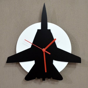 Könnte beinhalten: Eine schwarze Silhouette eines Düsenjägers mit roten Uhrzeigern auf einem weißen runden Hintergrund. Die Uhr ist an einer Wand montiert.