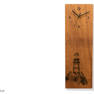 May include: A wooden wall clock with a lighthouse and houses engraved on the face. The clock has black hands and black numbers. The clock is made of light brown wood.