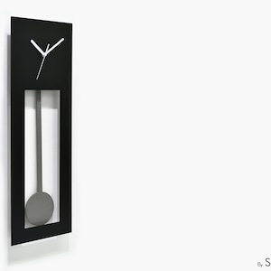 Puede incluir: Un reloj de pared negro moderno con péndulo. El reloj tiene un marco rectangular con una esfera blanca y manecillas blancas. El péndulo es gris y cuelga dentro del marco. El reloj está montado en una pared blanca.