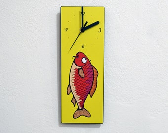 May include: A yellow clock with a red and purple fish design. The clock face has black hands and black numbers.